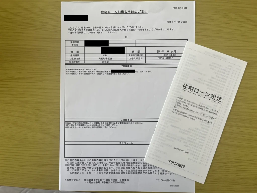 机の上に置かれたイオン銀行の住宅ローンお借入手続きのご案内と住宅ローン規定。
