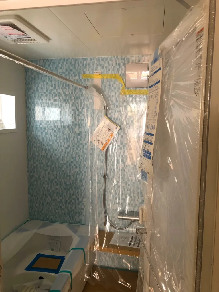 施工中の浴室ユニット内部で、壁や浴槽が養生されシャワー設備が取り付けられている
