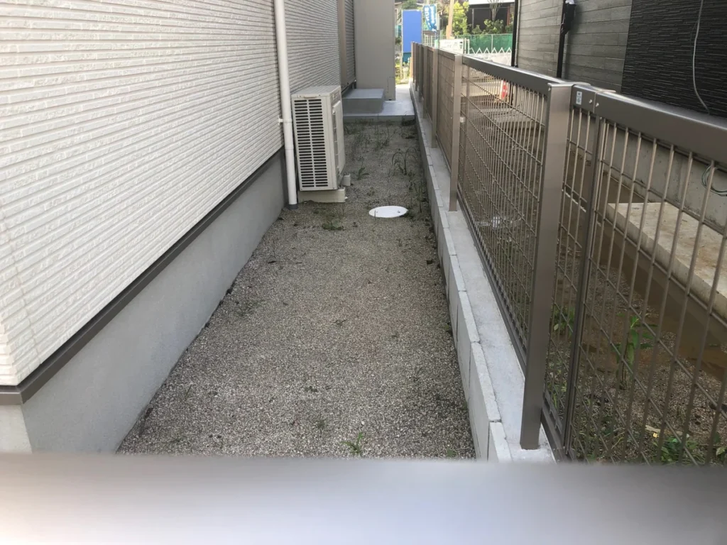 住宅脇の砂利敷き通路と境界フェンス
