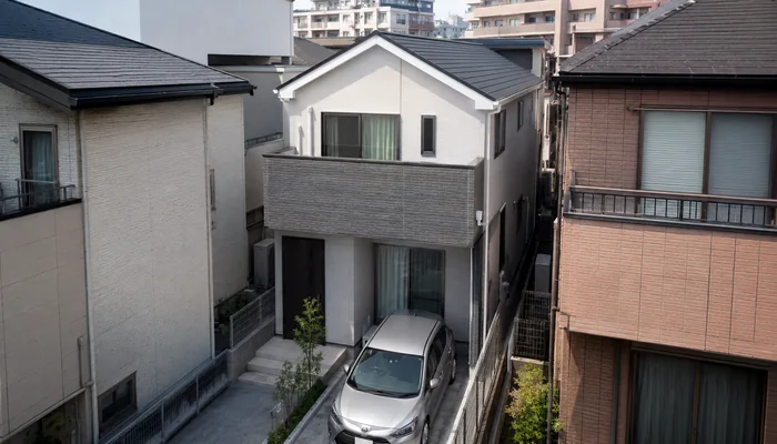 隣家との間隔が狭い敷地に建つ2階建て住宅と駐車中の車