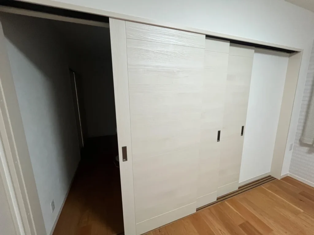 部屋の開口部を一部開けた白木調の三枚引き戸