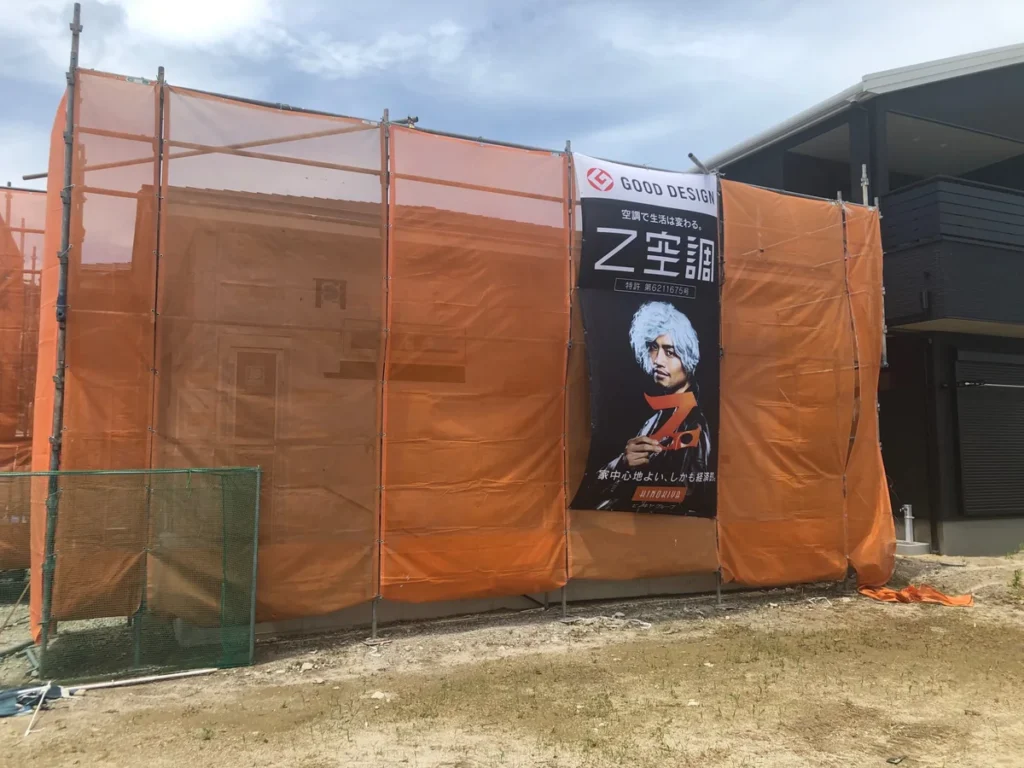 オレンジ色の養生シートに覆われ、Z空調の看板が掲げられた建築中の住宅外観