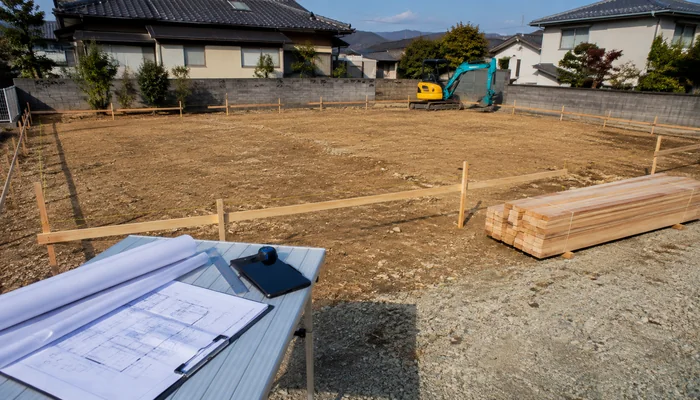 着工前の住宅建築予定地に置かれた設計図と小型重機