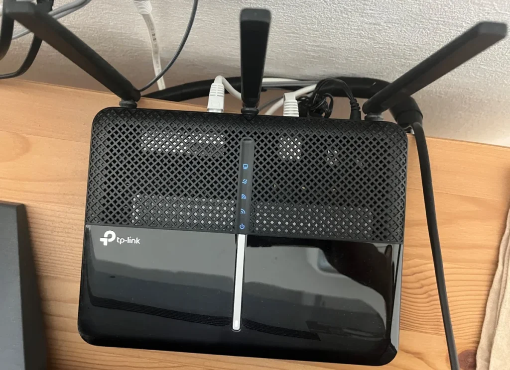 壁際の棚に設置されたTP-Linkの黒いWi-Fiルーター