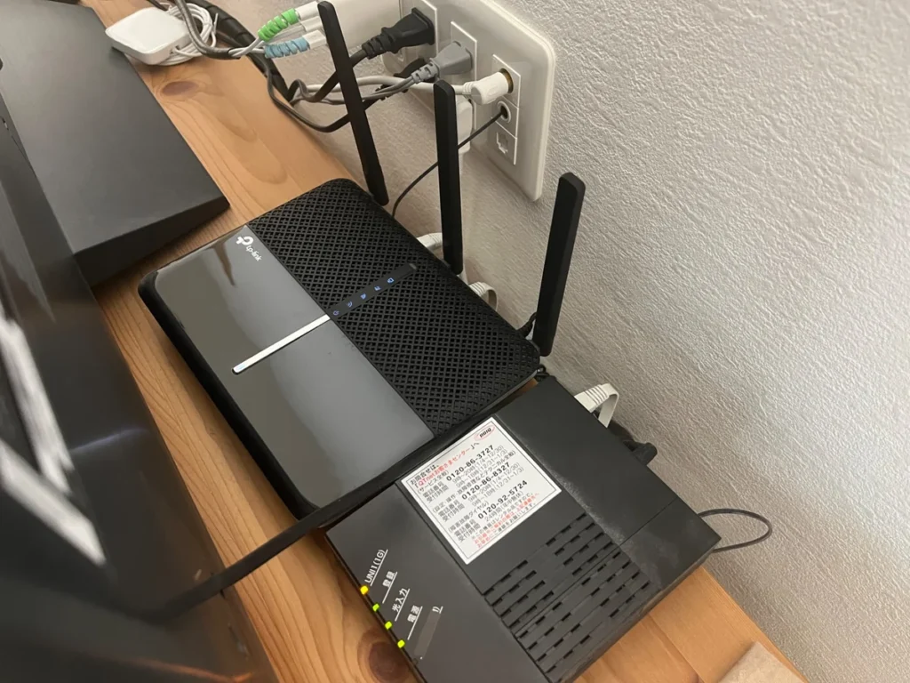 TP-LinkのWi-Fiルーターと光回線機器が壁際の棚に並んで接続されている様子
