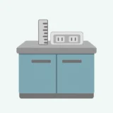 水色のカップボードの天板に、二口コンセントと縦向きの定規を並べたイラスト