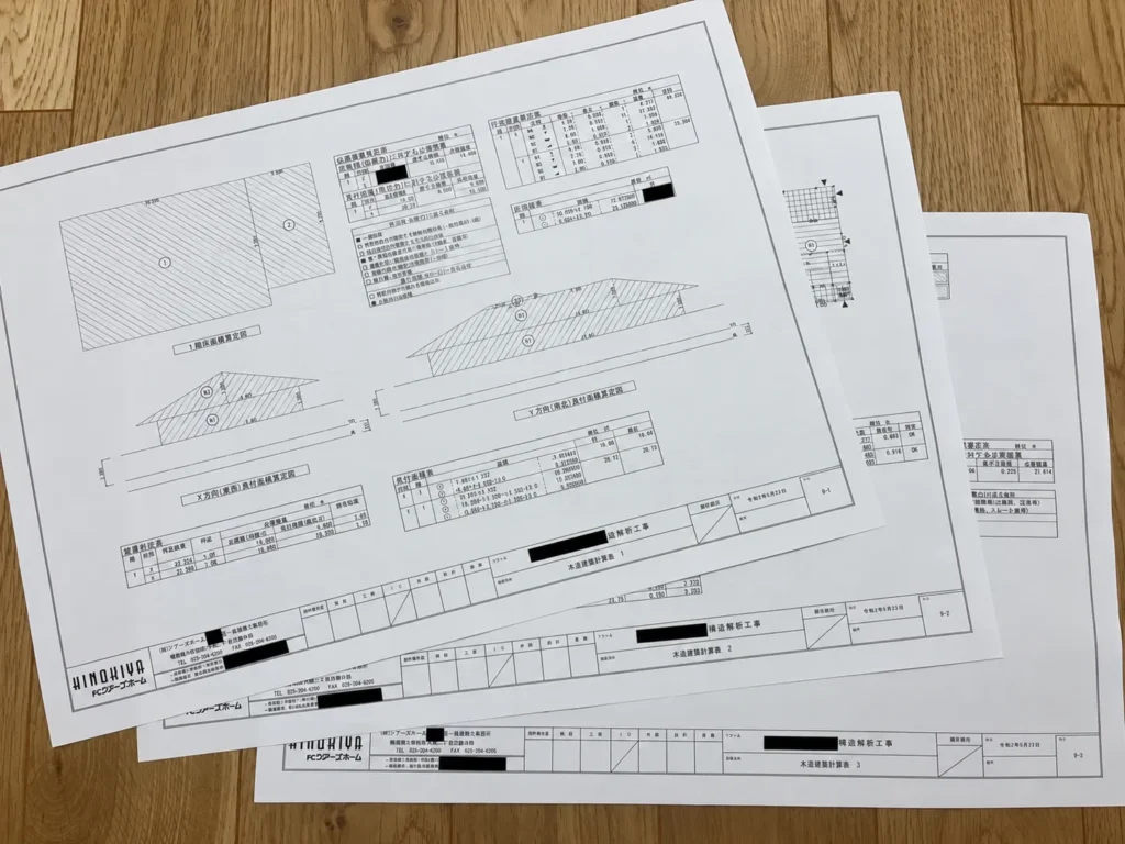 木目の上に3枚重ねて置かれた木造壁量計算表。斜線入りの算定図と数値表が写っている