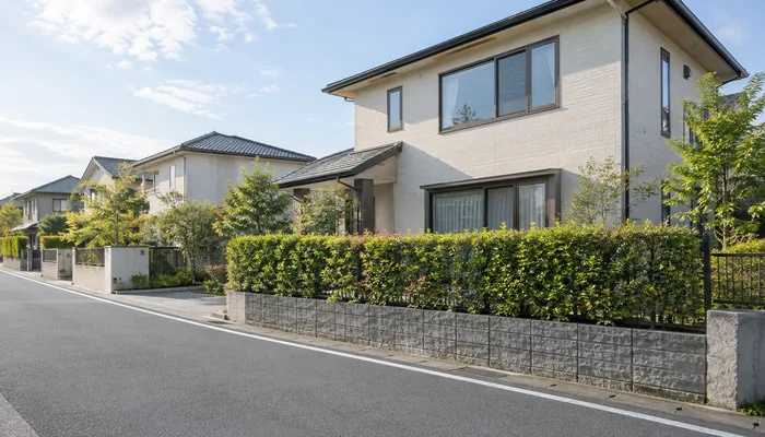 道路沿いの戸建ての前に、生垣と低い塀が続いている