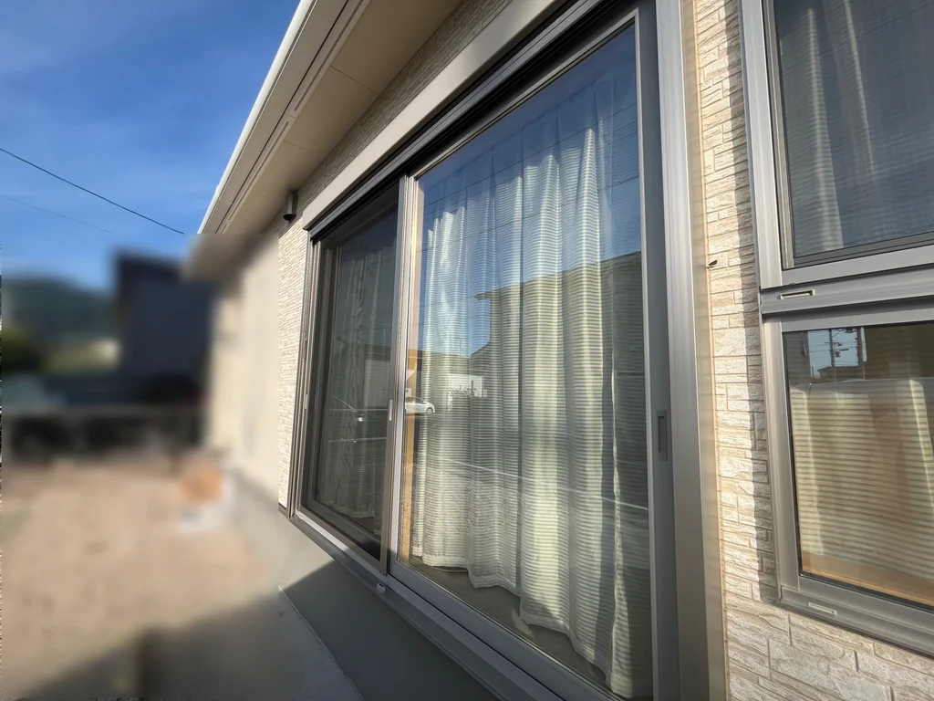 屋外から斜めに見た大きな2枚建ての引き違い窓。横にデザイン窓の一部が見える