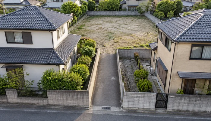 戸建ての間の細い通路が、奥の広い空き地につながっている
