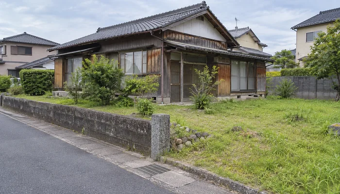 道路沿いの古い木造住宅の前に草の生えた庭と低い石塀が続いている