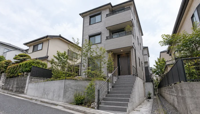 道路から三階建て住宅の玄関へ続くコンクリート階段と金属手すりを見上げる