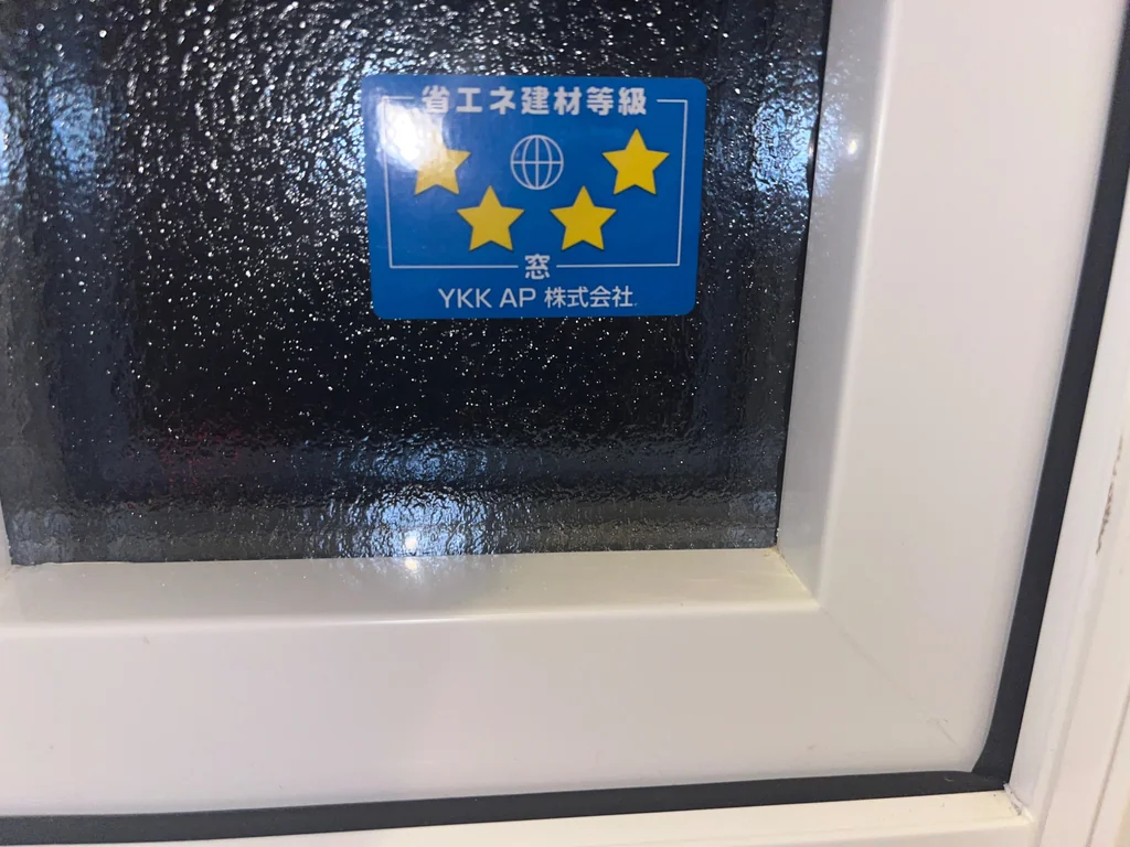 白い窓枠に収まる凹凸のある型ガラスと、YKK APの省エネ建材等級4つ星のシール
